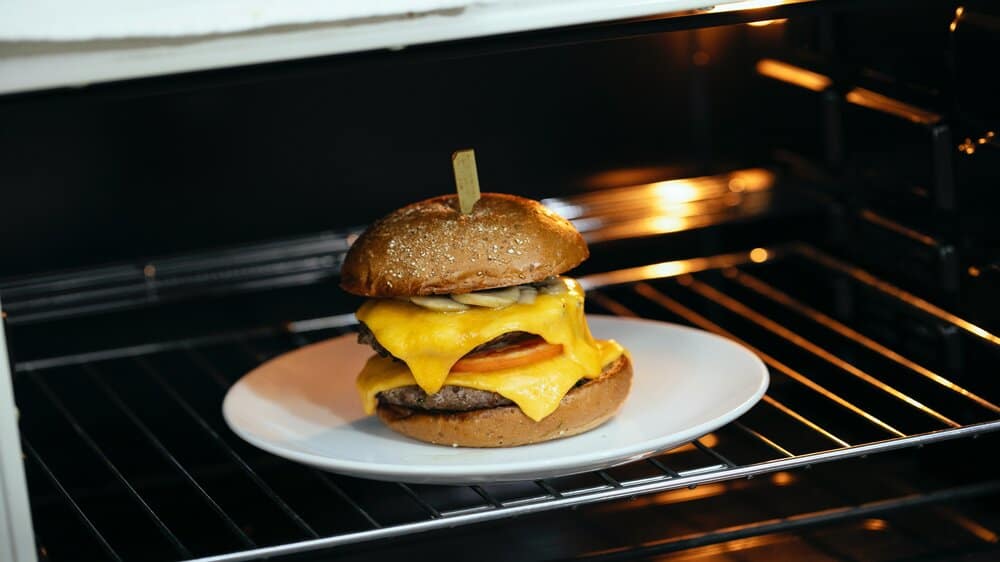 Een hamburger in de oven. Het ligt op een bordje op een ovenrooster.