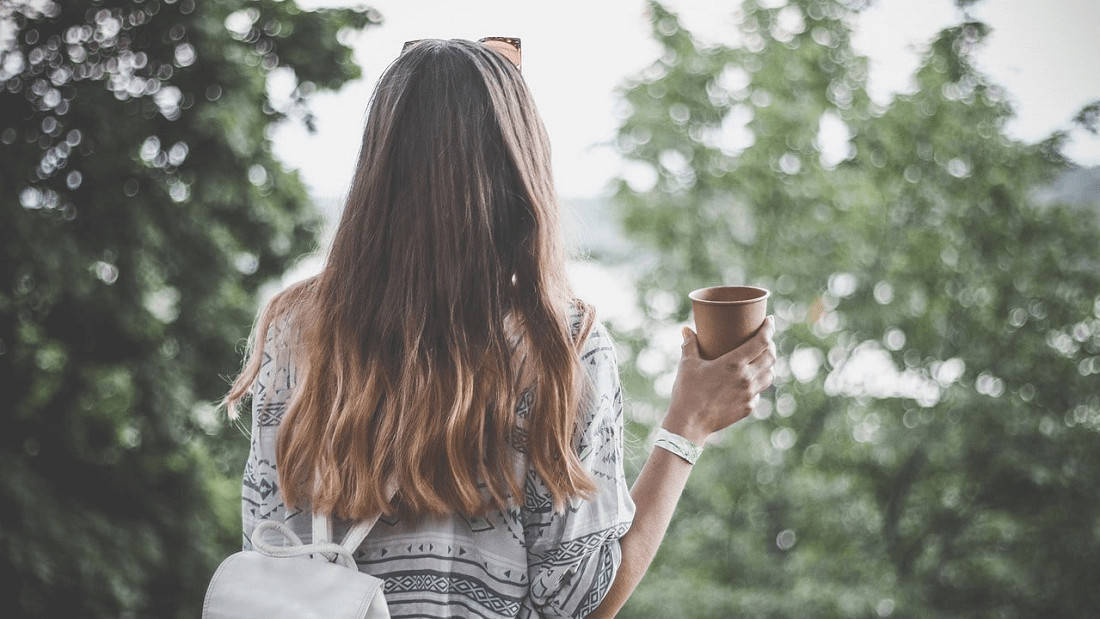 vrouw met lang haar en kop koffie in hand