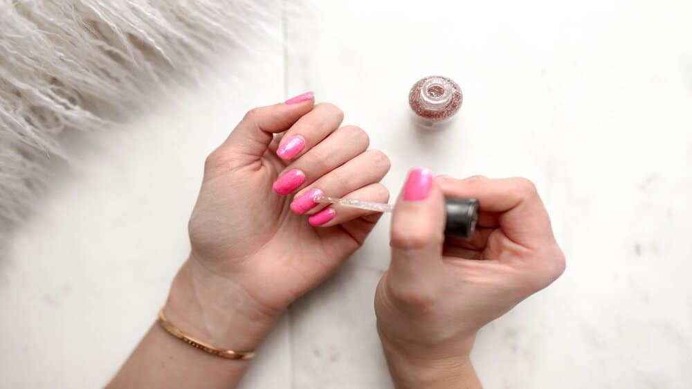 Vrouw lakt nagels met roze nagellak.