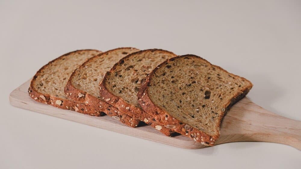 Een volkorenbrood op een broodplank, gesneden in vier sneetjes. Het brood heeft zaden.