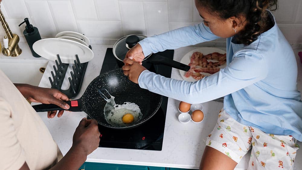 Kind helpt bij het bakken van een ei op een elektrische kookplaat