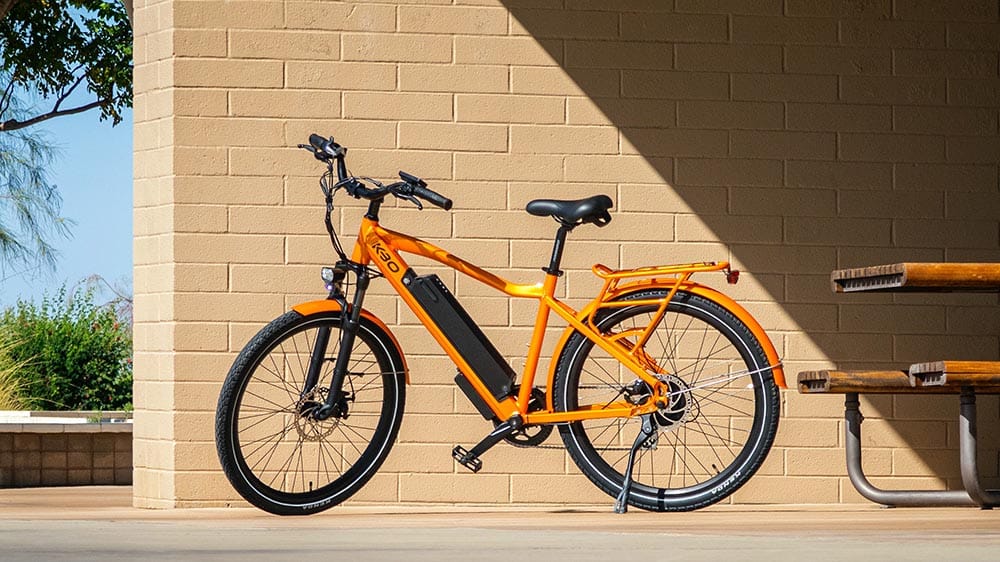 Een oranje elektrische fiets naast een muurtje