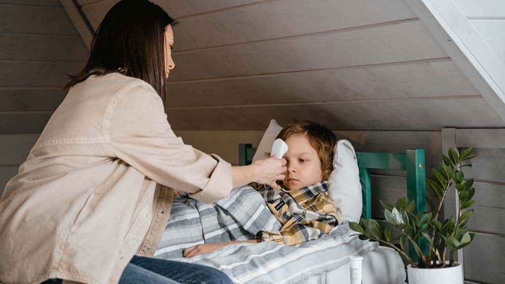 Moeder meet met een voorhoofdthermometer de temperatuur van een kind in bed.
