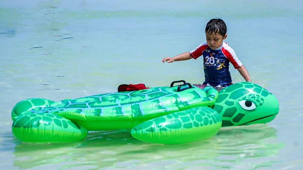 Kind met een opblaasschildpad in de zee.