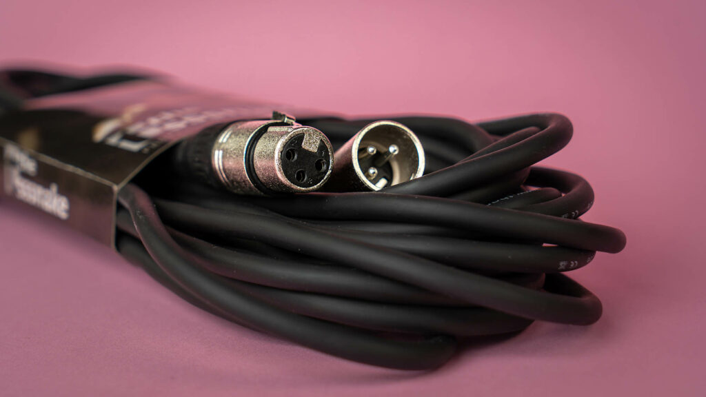Een zwarte, opgerolde XLR-kabel in een roze achtergrond