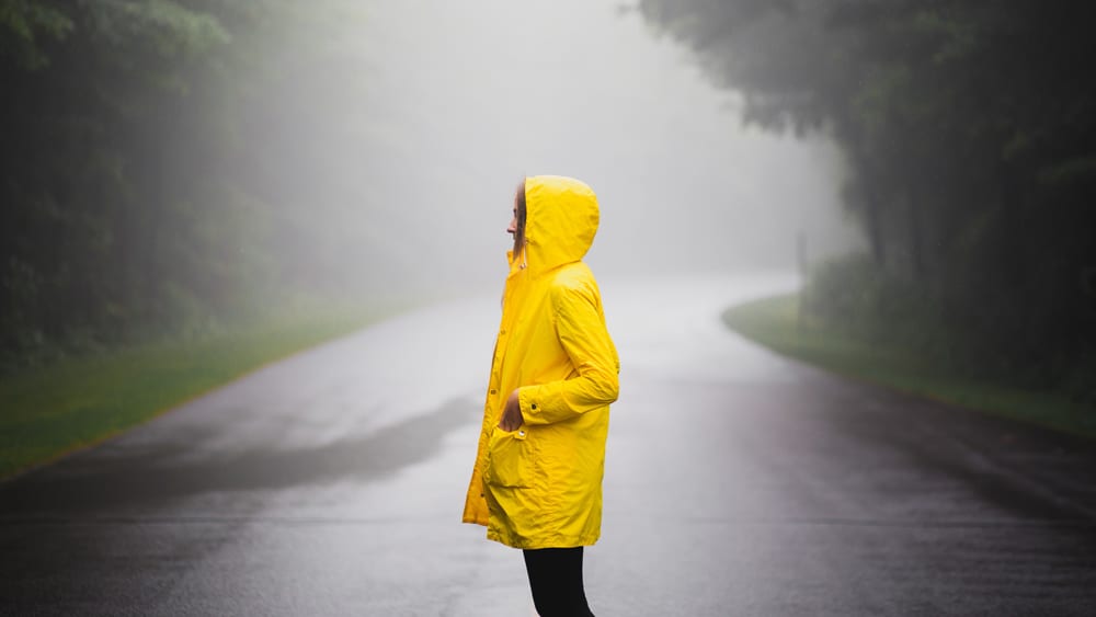 Vrouw staat in regen met geel regenpak