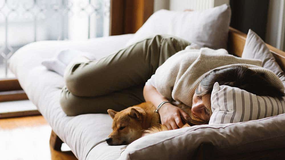 Vrouw ligt met hond op een slaapbank