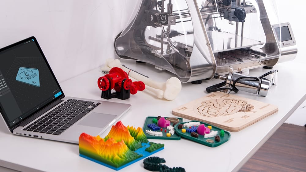 3D-printer op een bureau met een laptop en prints erbij.