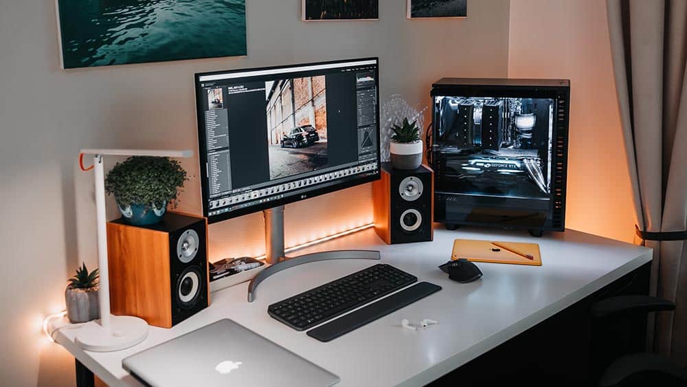 Een bureau met een computer, monitor, laptop en pc-speakers erop.