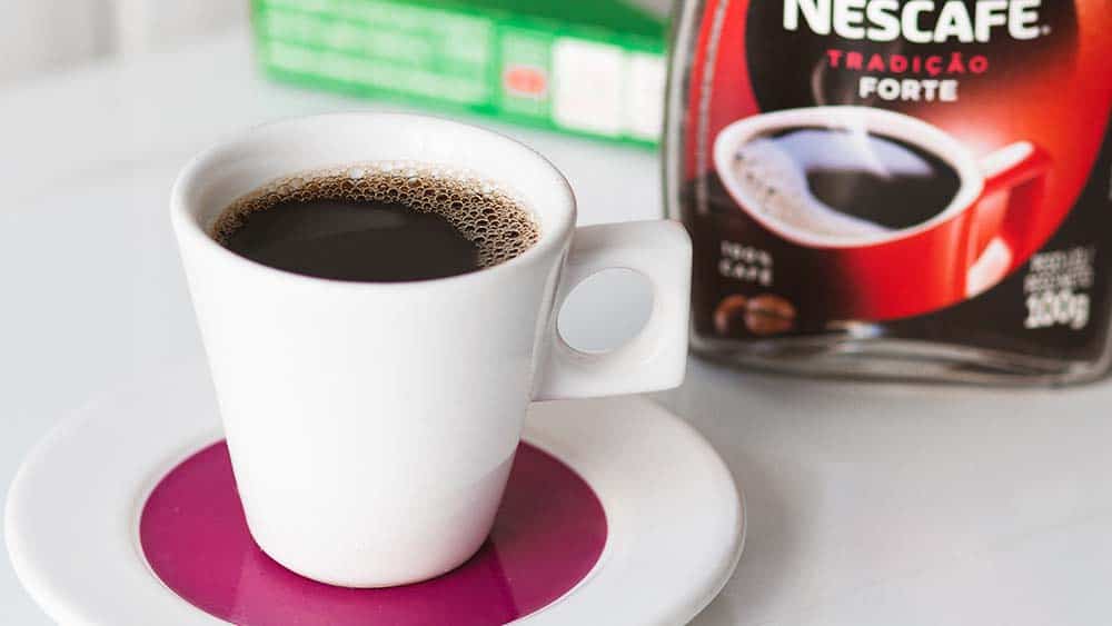Een kopje koffie met een pot oploskoffie ernaast van Nescafé