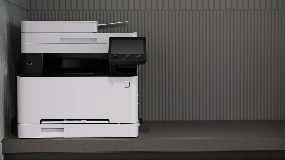 Een laserprinter staat op een bureau voor een grijze achtergrond