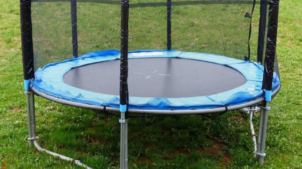 Kleine trampoline met net eromheen op een grasveld 