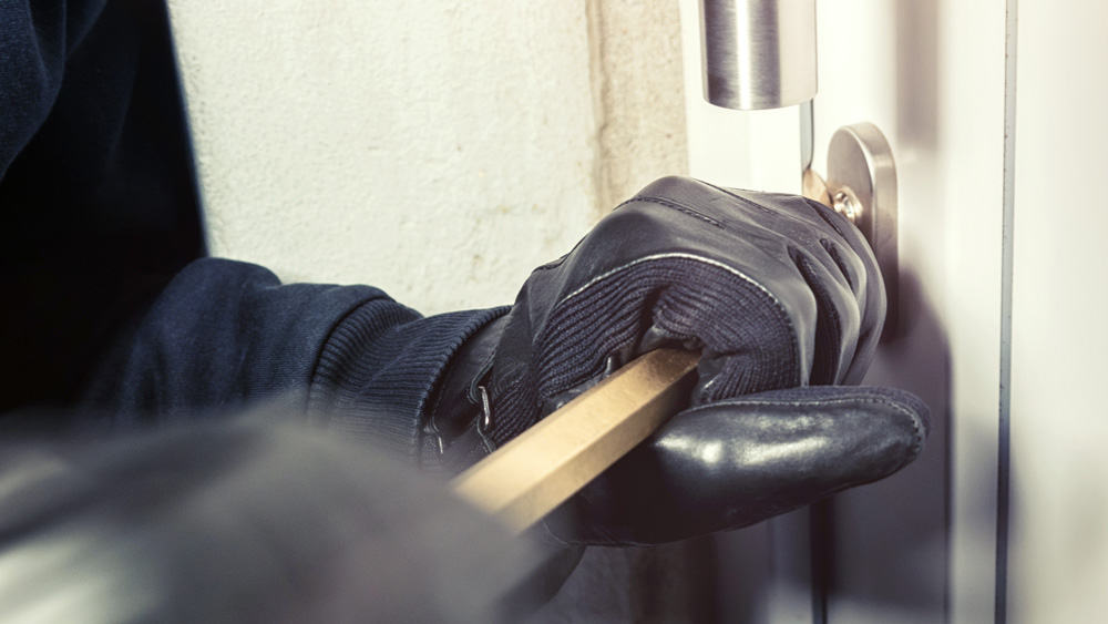 Een persoon met zwartleren handschoenen breekt een deur open met een koevoet