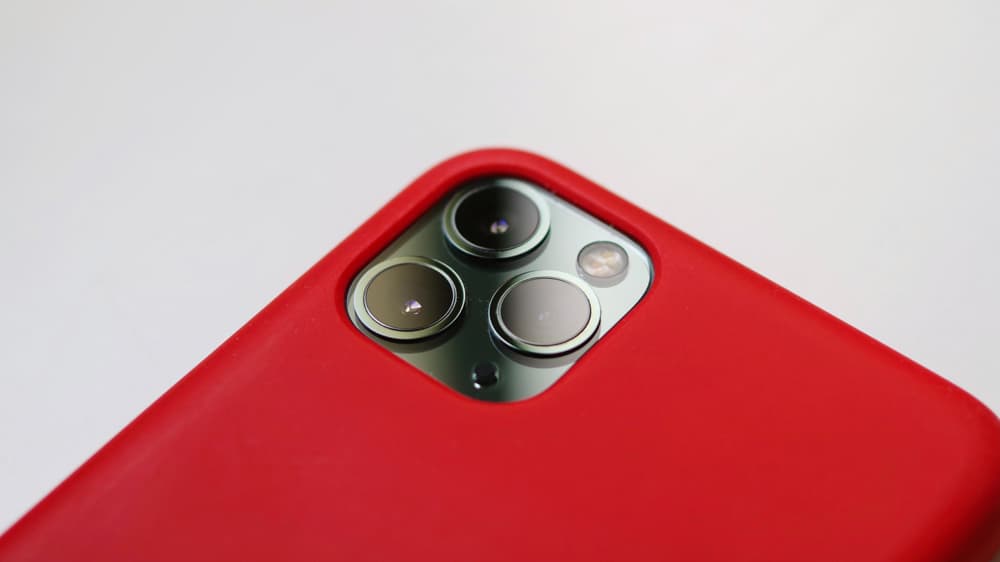 een close-up van een iPhone Pro met rood hoesje en drie lenzen.