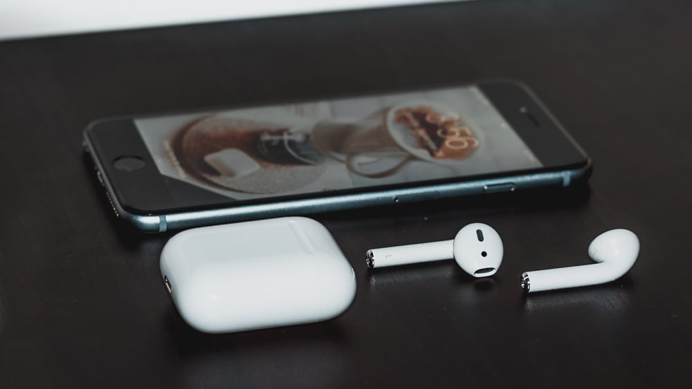 Een Iphone en AirPods liggen naast elkaar op een zwarte tafel