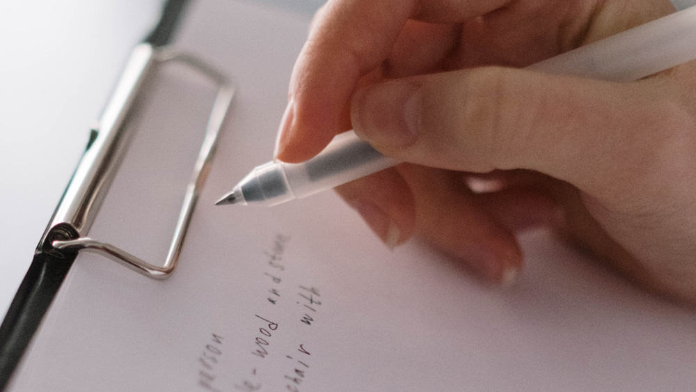 persoon schrijft met pen op een klembord
