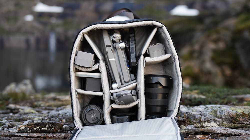 een camerarugzak met verschillende compartimenten waar lenzen, accessoires en een statief in zit