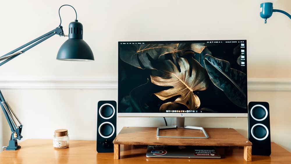 een monitor staat op een bureau met aan weerszijden twee geluidsboxen
