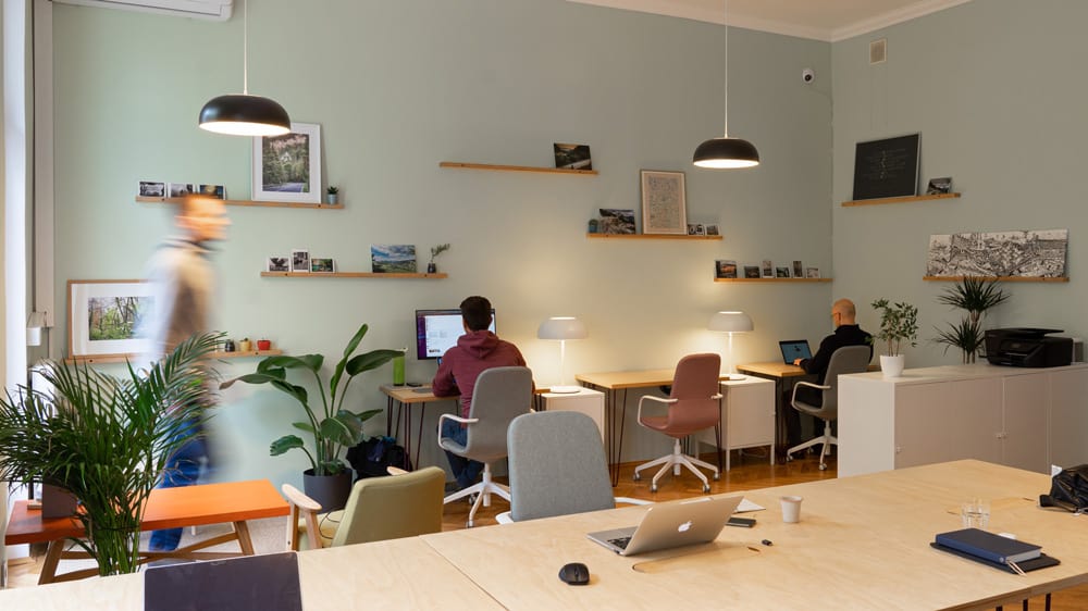 een kantoor met lichtgroene muur en verschillende mensen die op laptops werken.