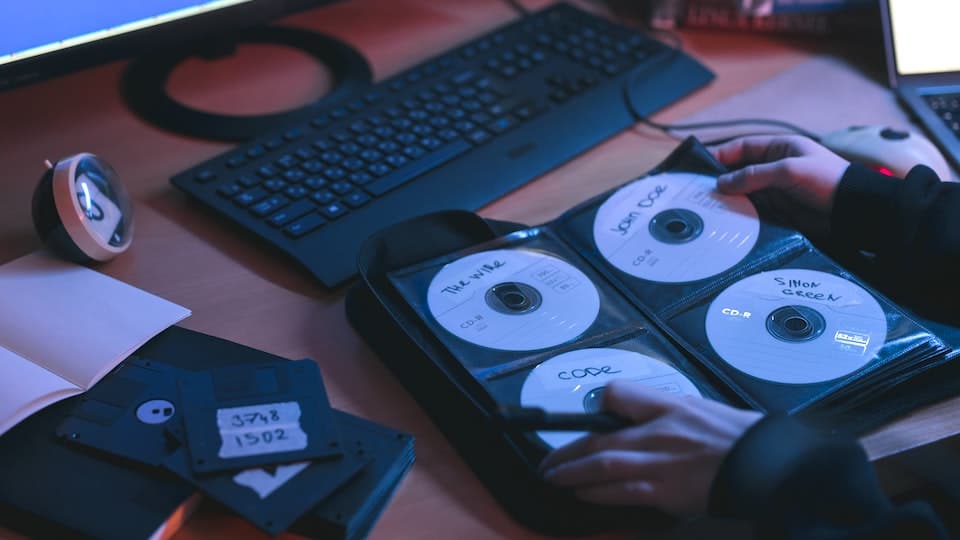 een persoon kijkt naar een map met cd's op een bureau, waar ook een toetsenbord en een optische drive ligt 