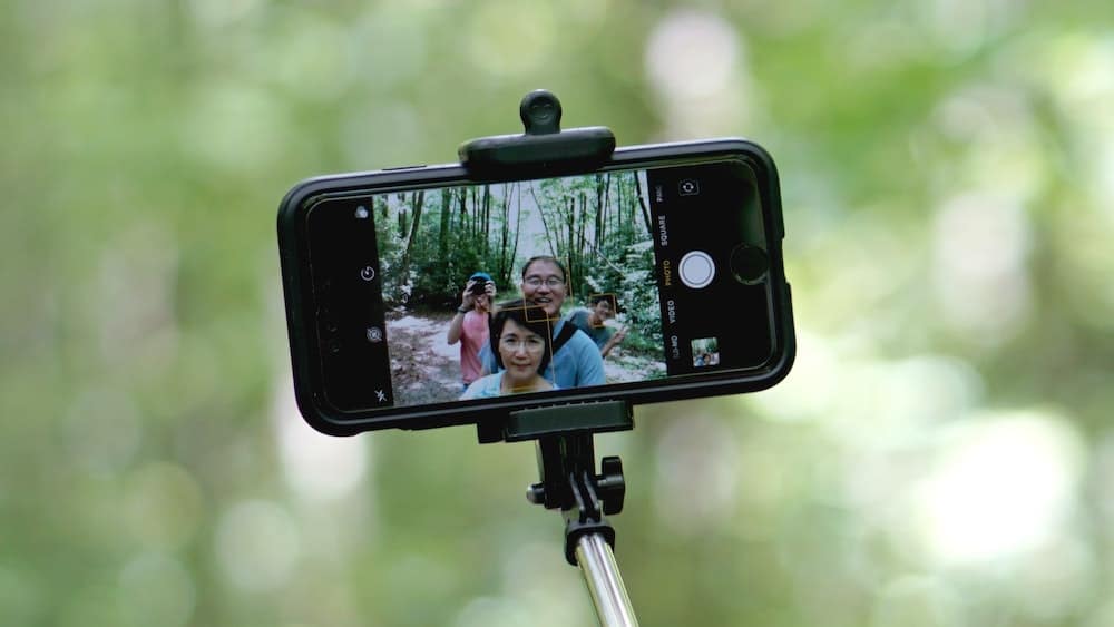een persoon gebruikt een smartphone op een selfie stick om een groepsfoto te nemen