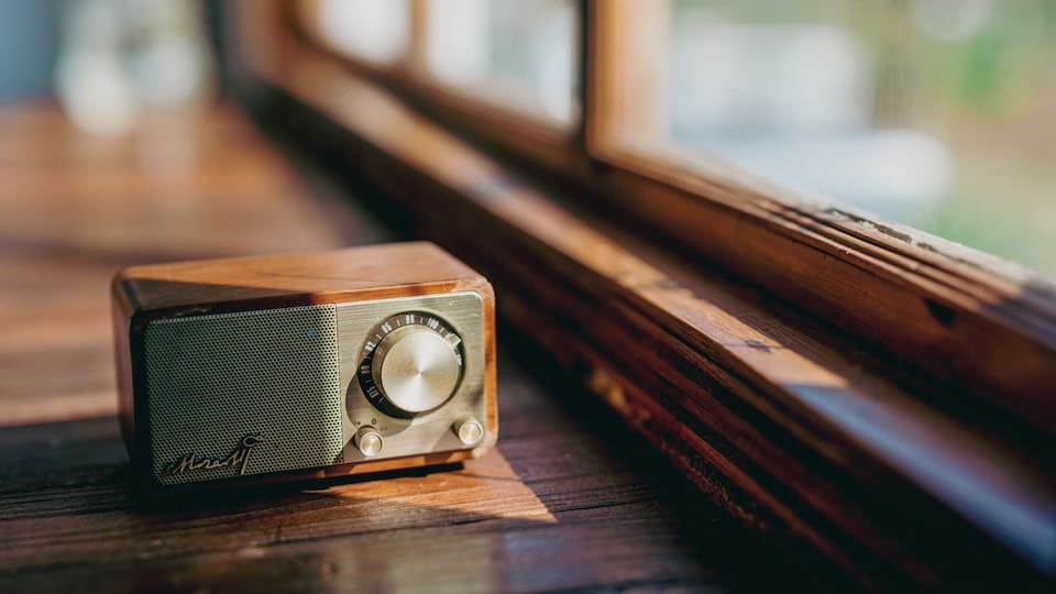 Een kleine radio staat bij een houten raamkozijn.